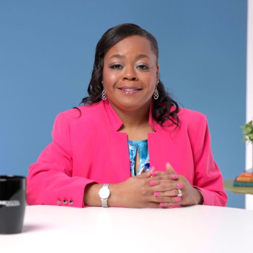 A professional woman with expertly styled hair and makeup smiles with confidence for the camera at her desk for a branding photoshoot.