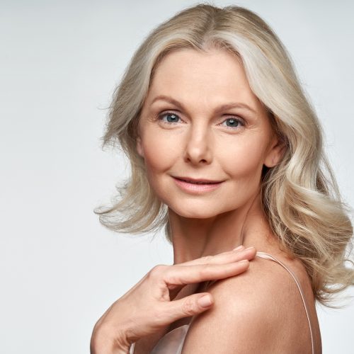 Attractive gorgeous mature older woman looking at camera isolated on white background advertising skincare spa treatment. Mid age tightening face skin care rejuvenation cosmetics concept. Portrait