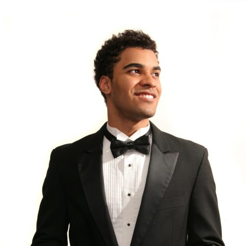 A young man in a tuxedo smiles confidently.